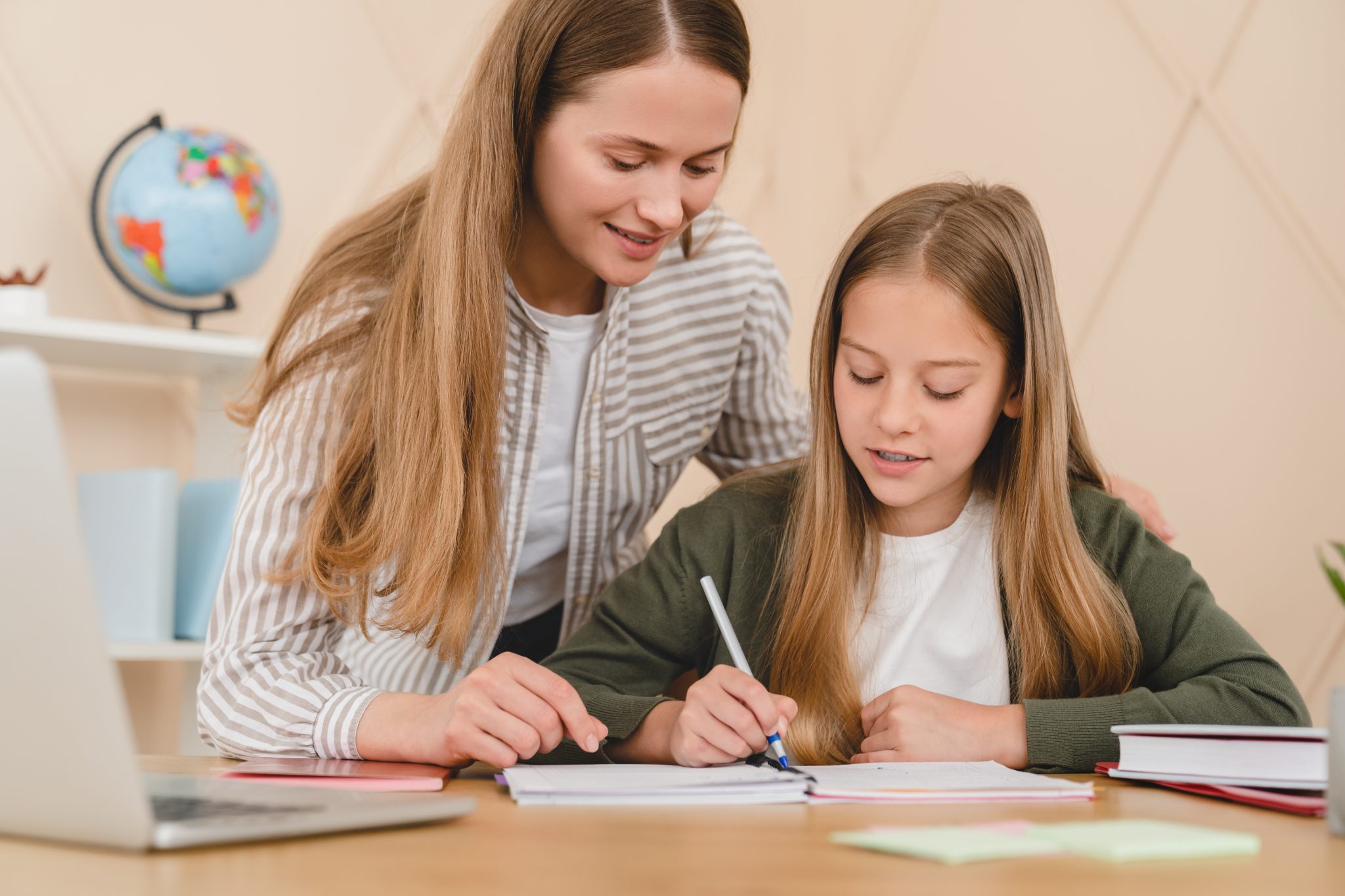Student-tutoring.-Young-female-helping-child-write-in-book-on-desk-with-laptop-visible-shutterstock_2064776756-scaled